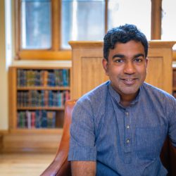 A picture of Sujit Sivasundaram, Professor of World History at the University of Cambridge, the 2025 Innes Lecture speaker, seated in a library.
